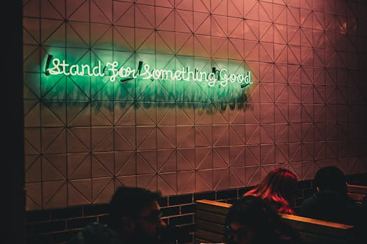 Green neon sign "Stand For Something Good" on a geometric tiled wall interior.