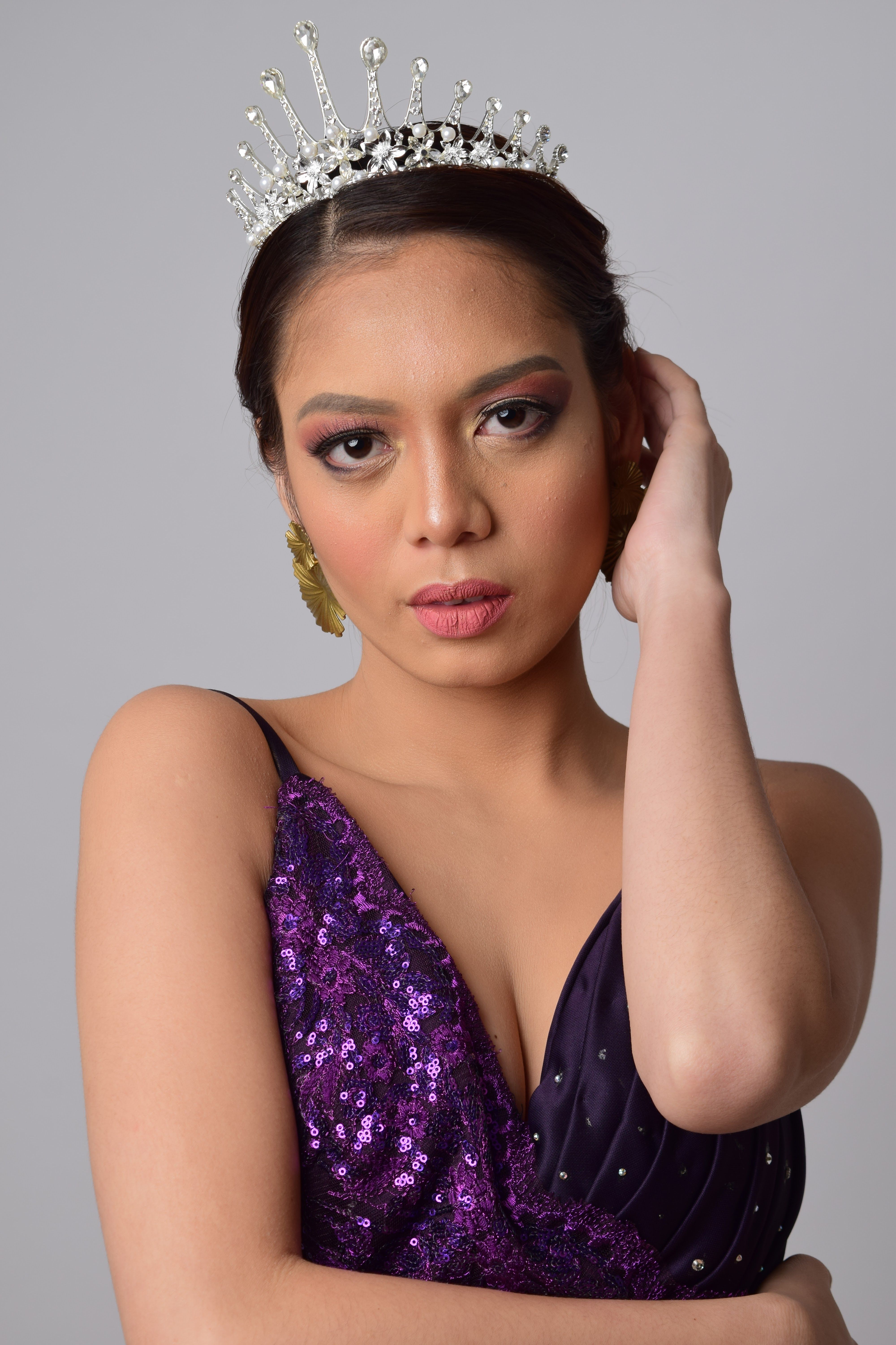 Glamorous woman wearing a tiara and purple dress poses gracefully indoors.