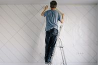 Faceless house painter undercoating wall in bright room