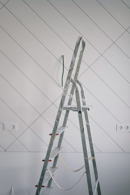 Tall gray metallic ladder covered with sports of white dry next to simple wall painted with slanted lines