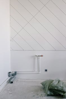 空房间肮脏的地板上散落着垃圾和枕头，白墙上覆盖着散热器管道的长而细的黑色斜线