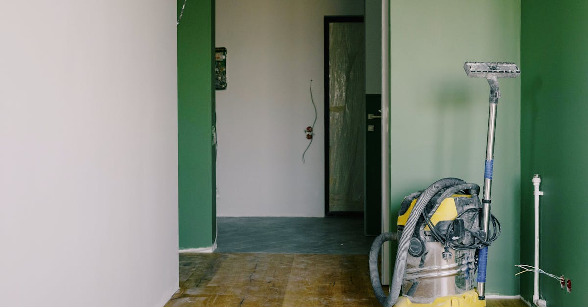 Industrial vacuum cleaner placed on dirty parquet in room with green walls and doorway in spacious apartment during repair works