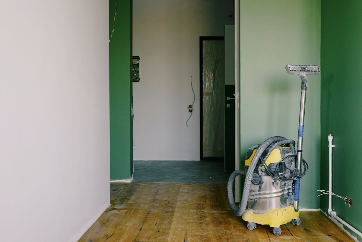 Industrial vacuum cleaner placed on dirty parquet in room with green walls and doorway in spacious apartment during repair works