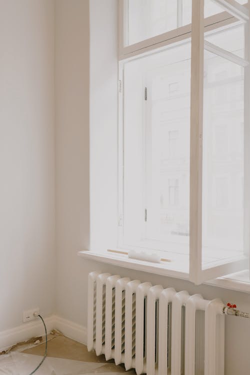 Interior of light room with open white window with instruments on windowsill over battery in apartment with white wall during repair works