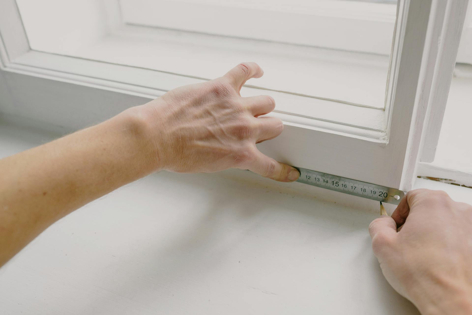 From above of crop anonymous workman measuring wooden window frame using metal ruler and pencil in house