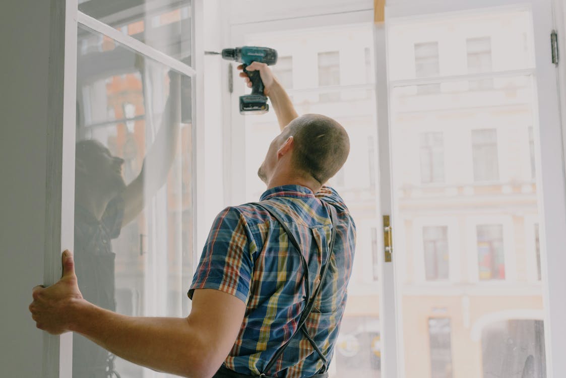 Handyman installing window frame with drill in house