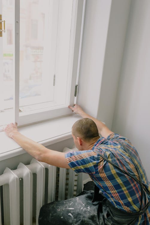 Free Back view of unrecognizable fitter in dirty apron installing window above radiator while doing home renovation Stock Photo