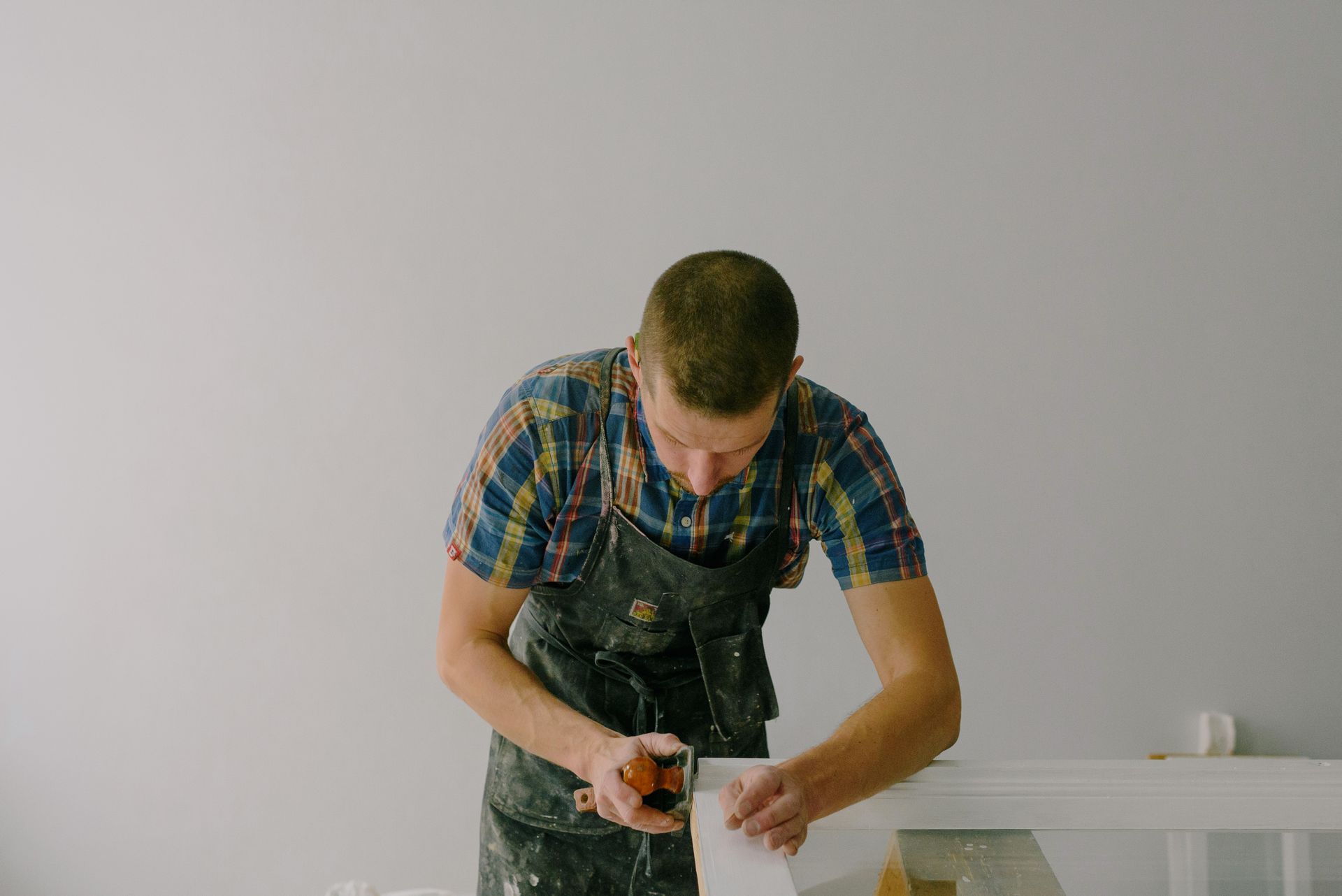 Concentrated anonymous joiner in apron working with wooden plank for furniture in light room