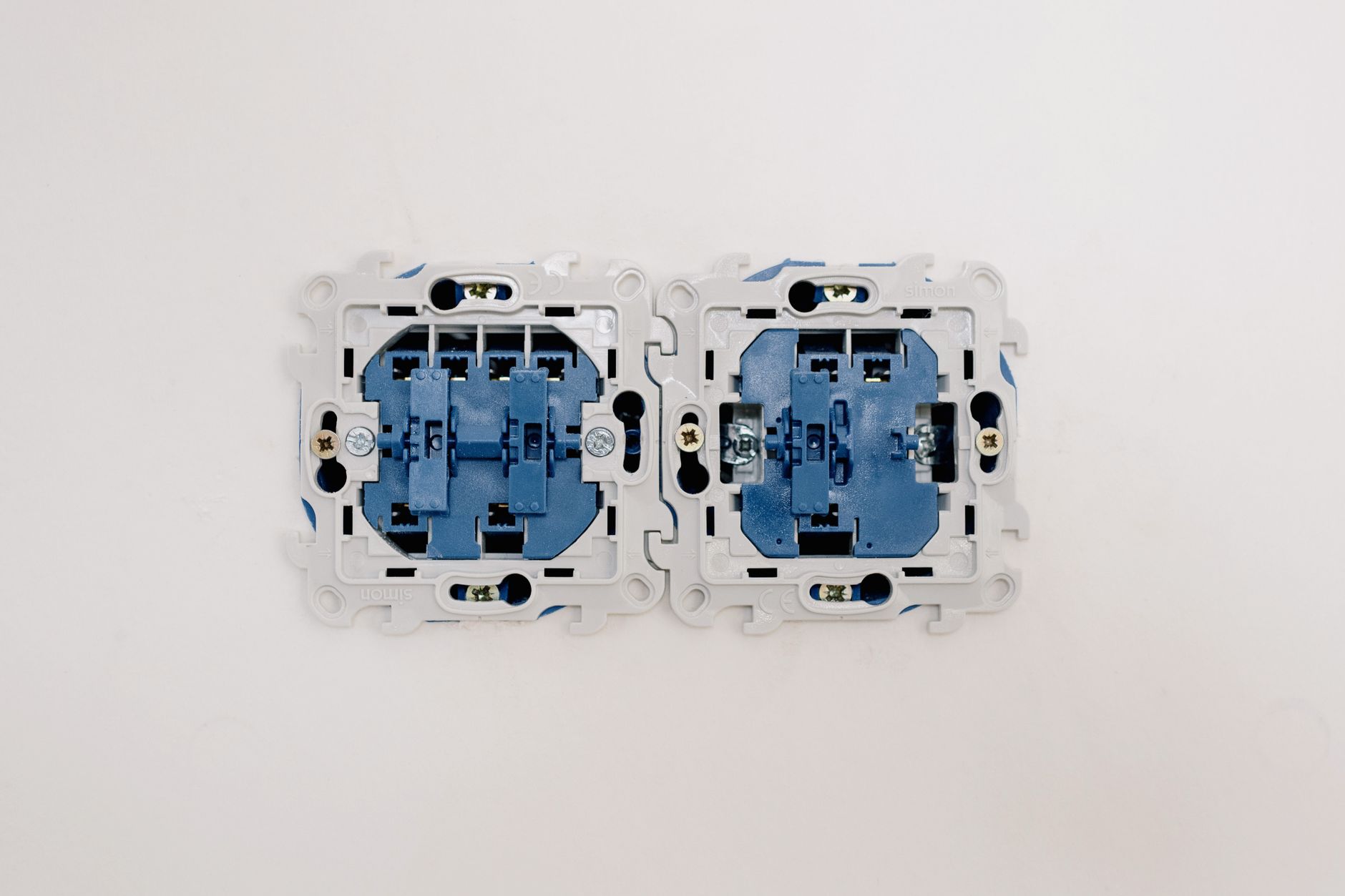 Opened electric switches without caps placed on light wall in apartment during repair works