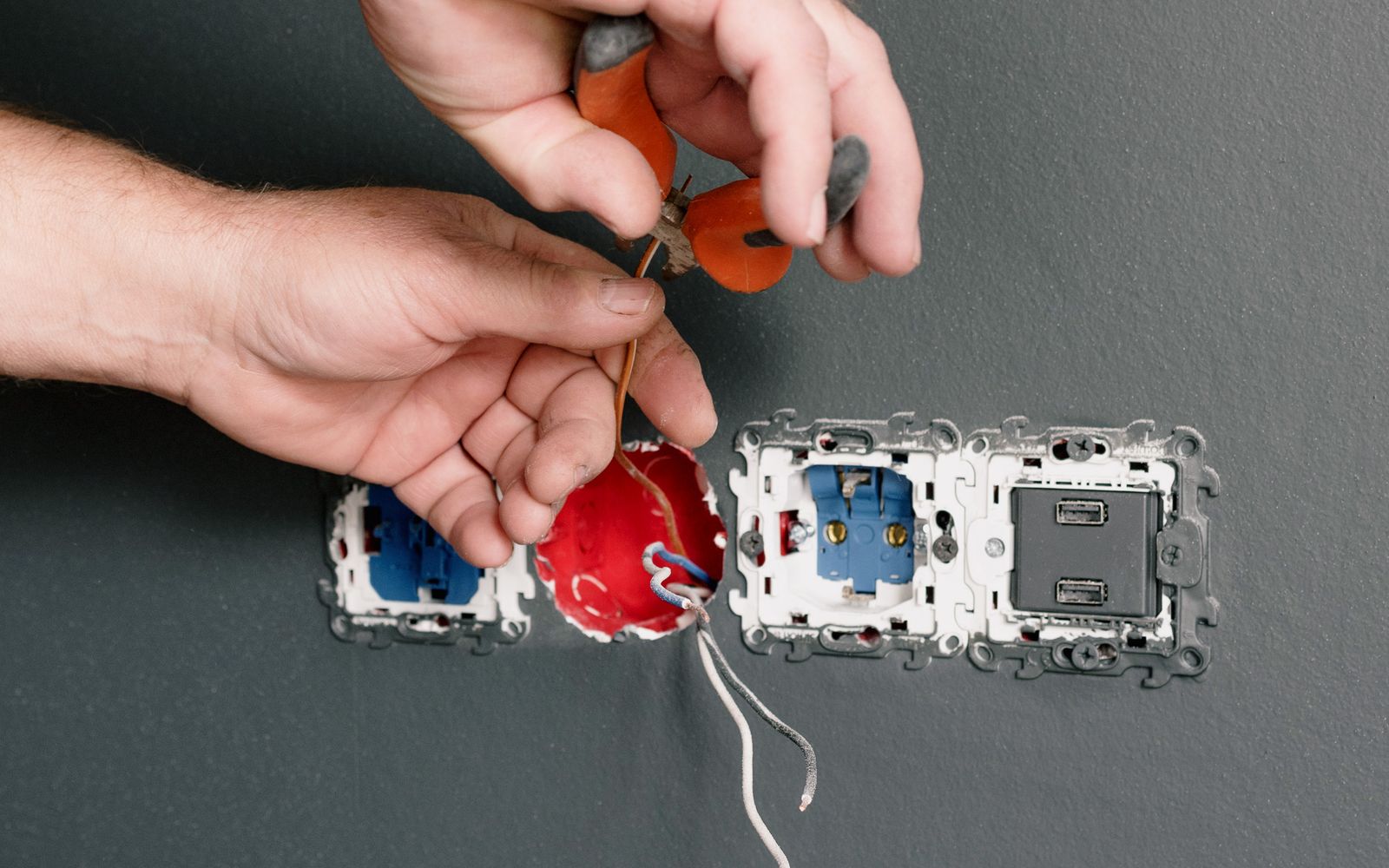An electrician fitting a wall socket in a room with grey walls