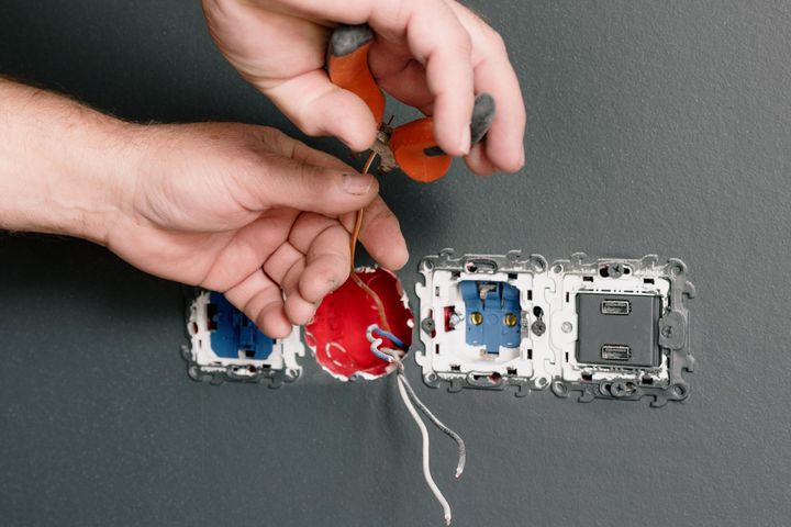 Electrician installing outlets and switches Electrician installing wall sockets and switches in a gray-walled room
