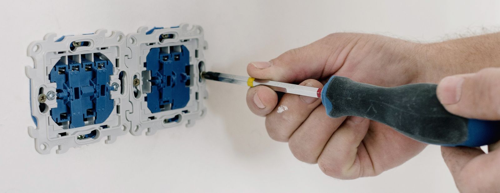 Hands using a screwdriver to install an electrical socket on a white wall