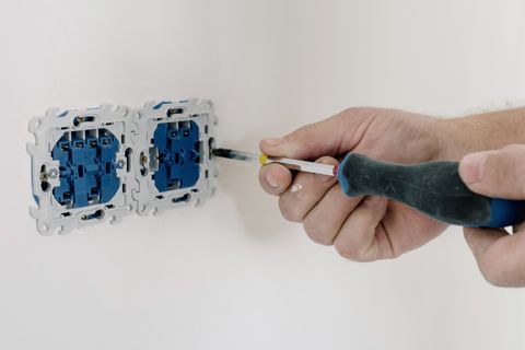 Hands using a screwdriver to install an electrical socket on a white wall