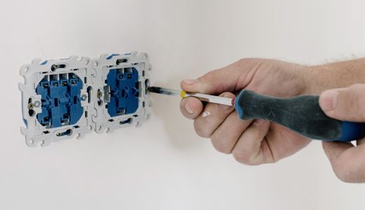 Hands using a screwdriver to install an electrical socket on a white wall