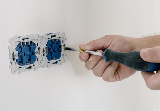 Hands using a screwdriver to install an electrical socket on a white wall