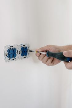 Crop faceless man using screwdriver for installation switches in apartment with light wall in daytime