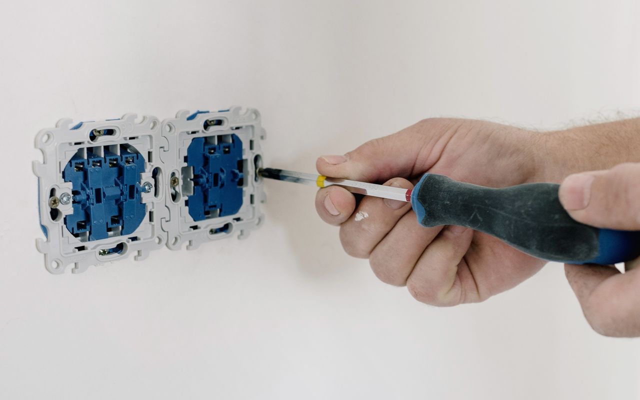 Hand with screwdriver fitting a double socket on a white wall