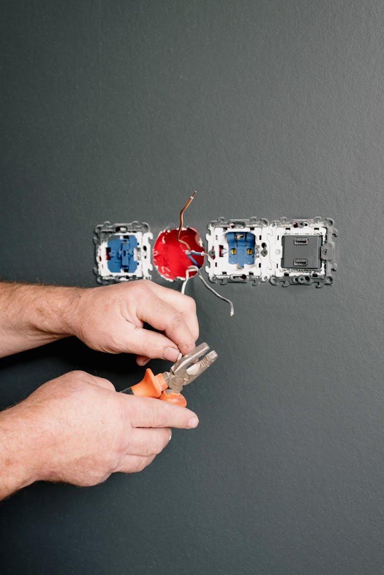 An Electrician Using Pliers To Repair The AC Power Plugs And Sockets