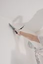 Crop unrecognizable male in gloves holding tool while standing on ladder and renovating walls in flat
