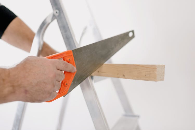 Crop Man Sawing Wooden Plank At Home