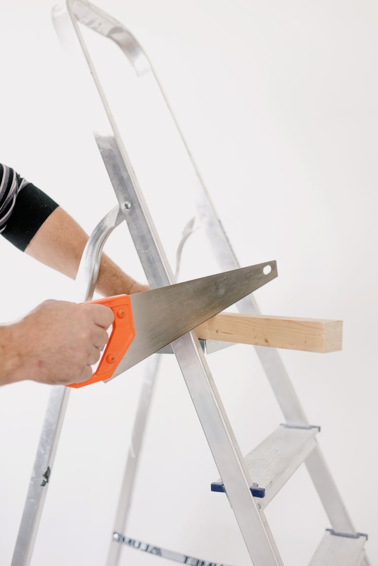 Crop Man Sawing Wooden Plank On Ladder