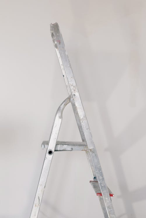 Metallic step ladder on floor against white wall in room during repair works