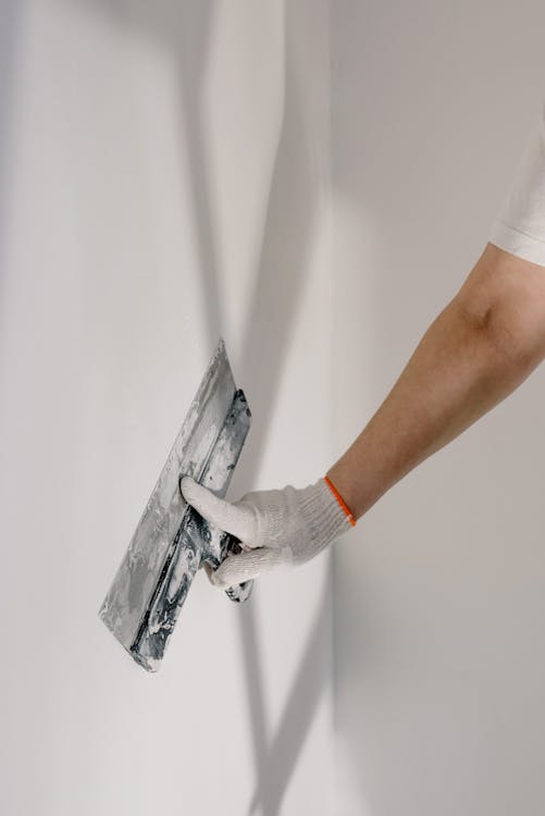 Free Crop anonymous male worker in gloves holding putty knife while working at home Stock Photo