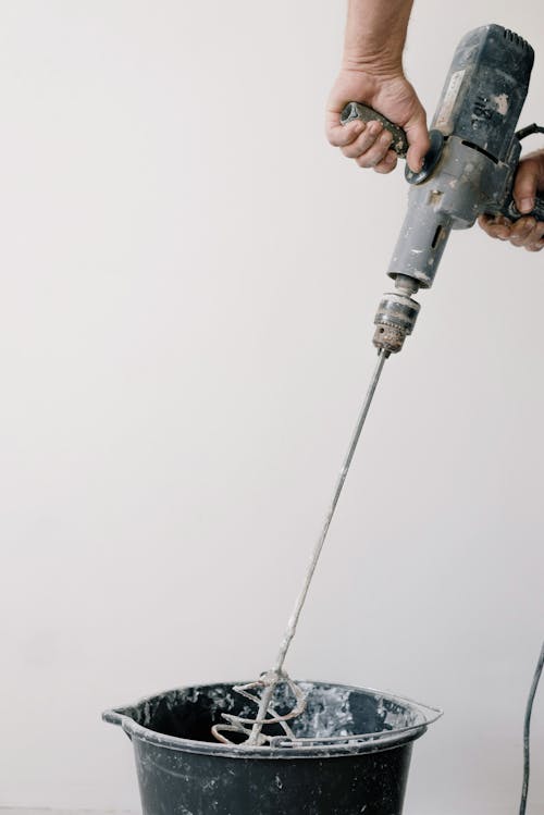 Free Crop unrecognizable male worker holding drill with tool and mixing cement in plastic container Stock Photo