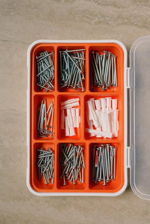 Top view of collection of different metal nails and plastic dowels in box on table