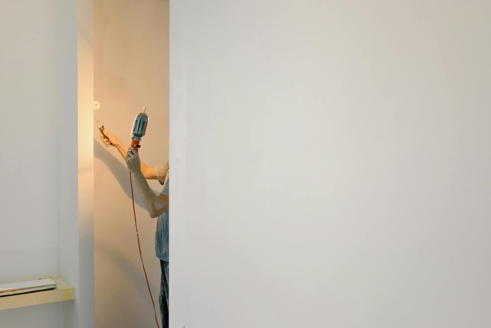 Unrecognizable person using a drill on a minimalist white wall in a home interior.