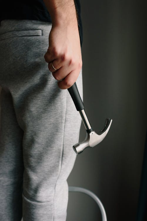 Crop unrecognizable male in casual clothes holding metal hammer with rubber handle in room