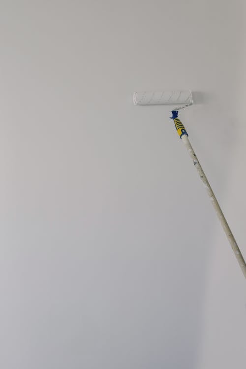 Paint roller with white acrylic paint on wall in room during renovation at home