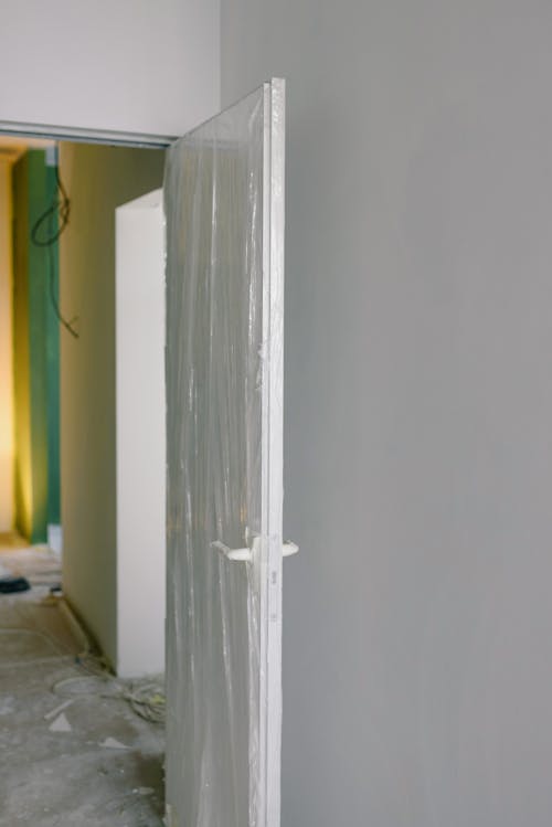 White wooden door wrapped in plastic and located in light empty apartment with white walls during redecoration