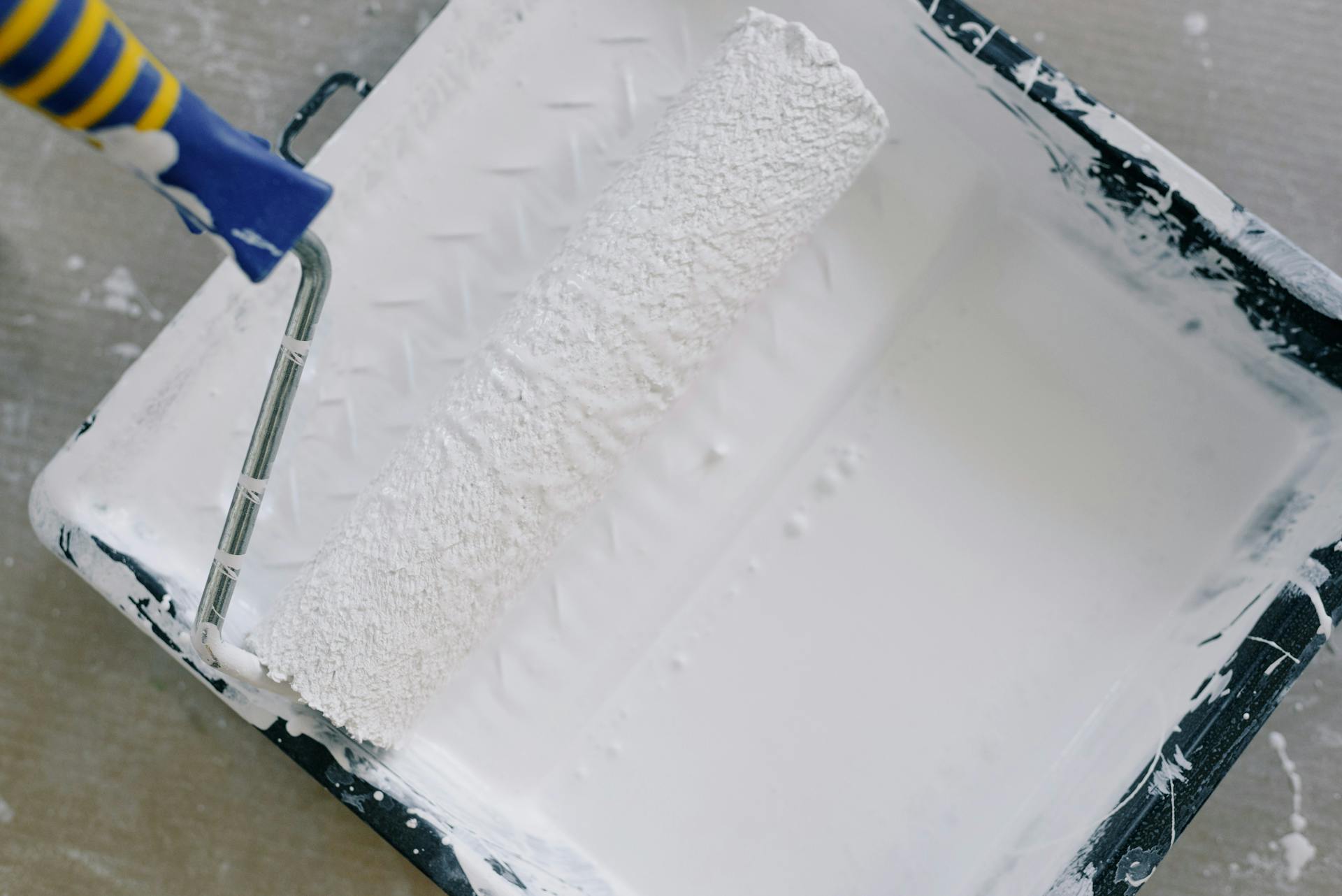 Top view paint roller placed in black tray filled with white pigment and placed on floor in renovating apartment