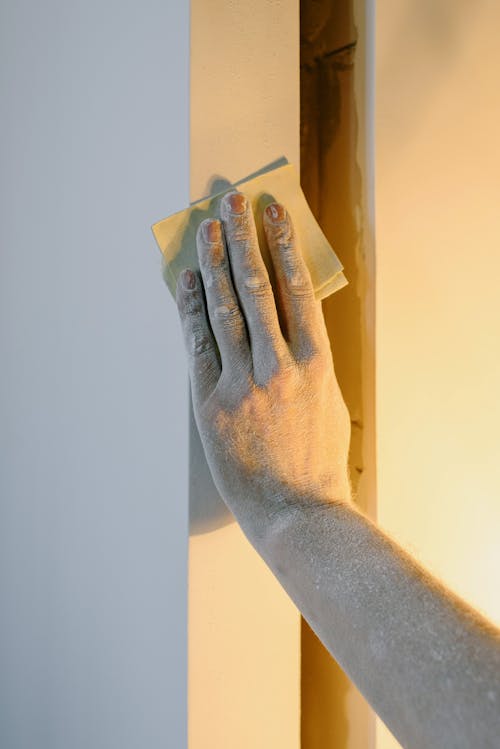 Crop faceless person grinding wall with sandpaper during renovation