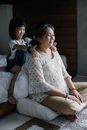 Positive Asian girl sitting on bed and massaging shoulders of mother sitting on floor in bedroom