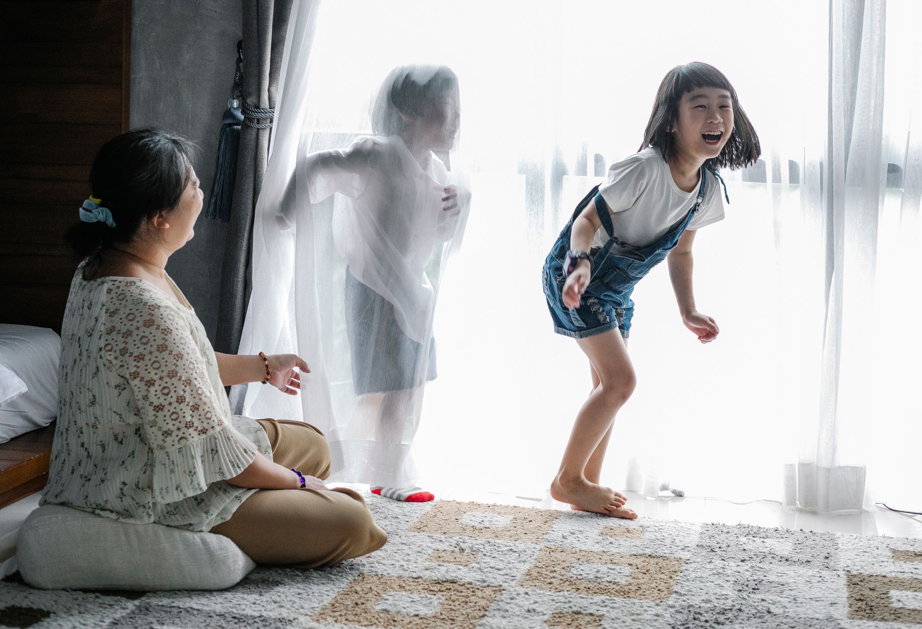 Mother sitting on floor and playing with kids near big window in light room