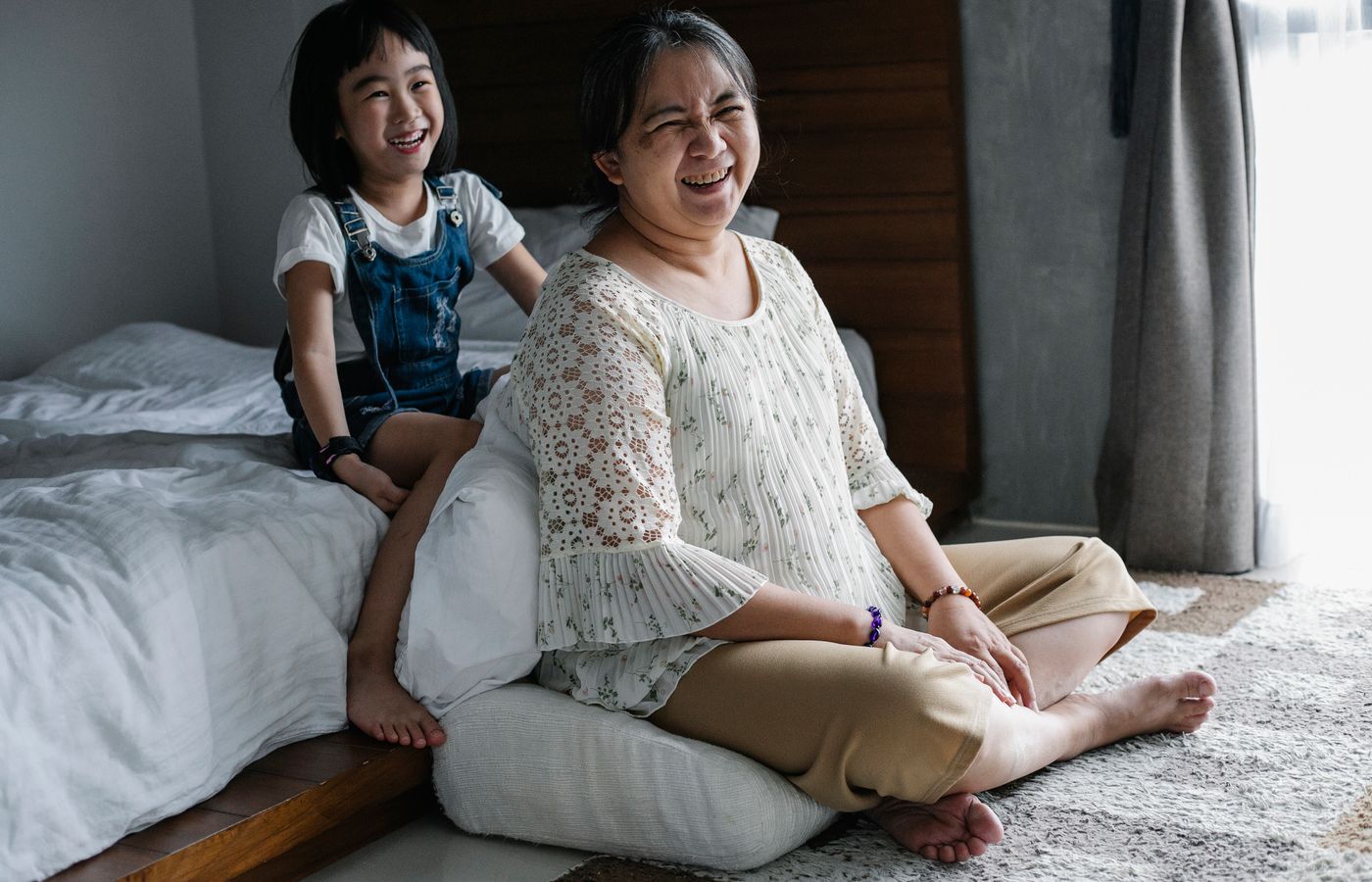 Joyful moment of a grandmother and granddaughter laughing together in the bedroom.