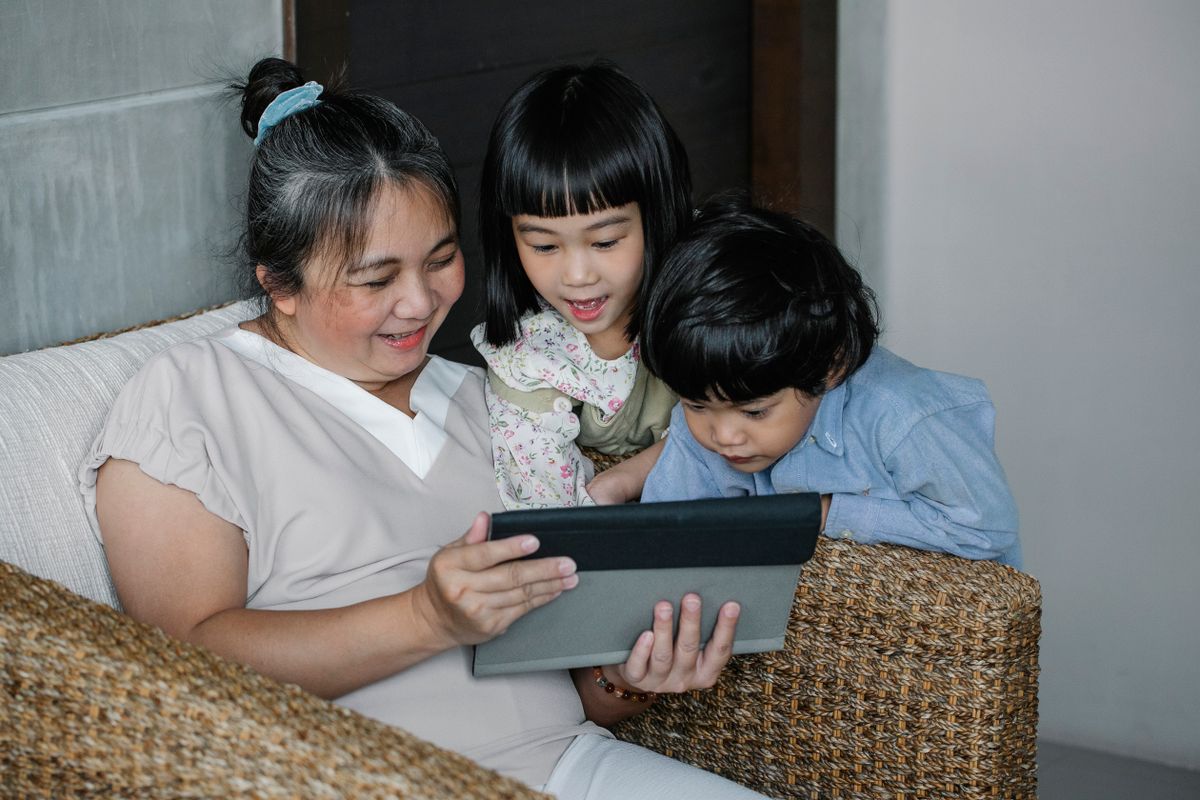 A grandmother sitting with children and using a tablet in a warm home setting