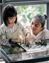 一个专注的亚洲孩子正和母亲在家里的玻璃桌旁下国际象棋