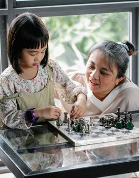 一个专注的亚洲孩子正和母亲在家里的玻璃桌旁下国际象棋