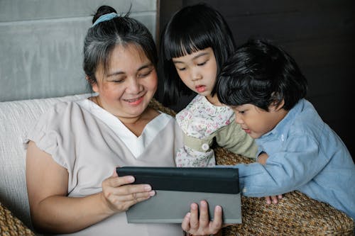 Free Positive Asian grandmother and kids looking at screen of  tablet while resting at home Stock Photo