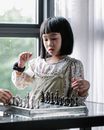 灯光室里，一位专注的亚洲女孩穿着休闲装，靠窗下棋，一边思考着下一步行动