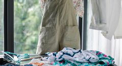 Crop faceless woman choosing outfit from clothes heap on table