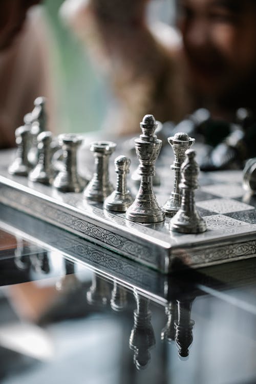 Classic metal chess board with set figurines designed with carved ornaments and placed on glass table in light room