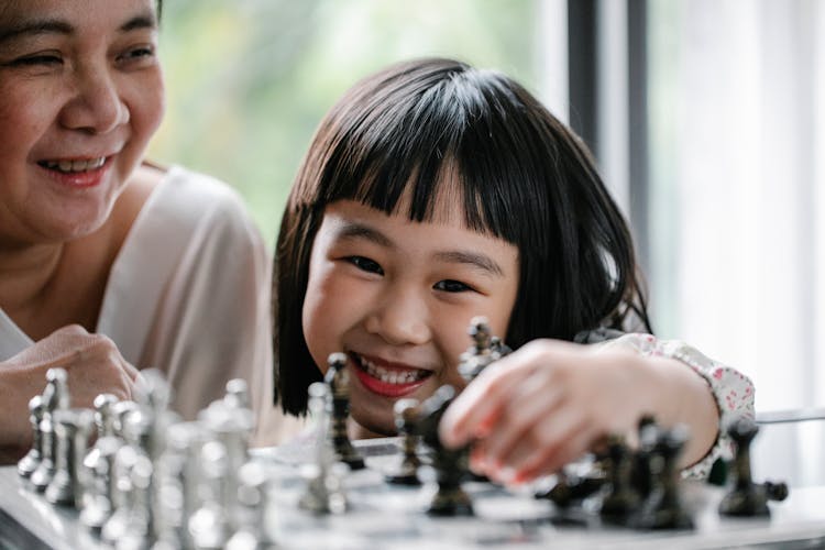 Happy Asian Girl With Grandmother Playing Chess