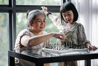 一位快乐的祖母和孙女在窗边下棋，共享亲密的室内时光