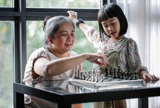 一位快乐的祖母和孙女在窗边下棋，共享亲密的室内时光