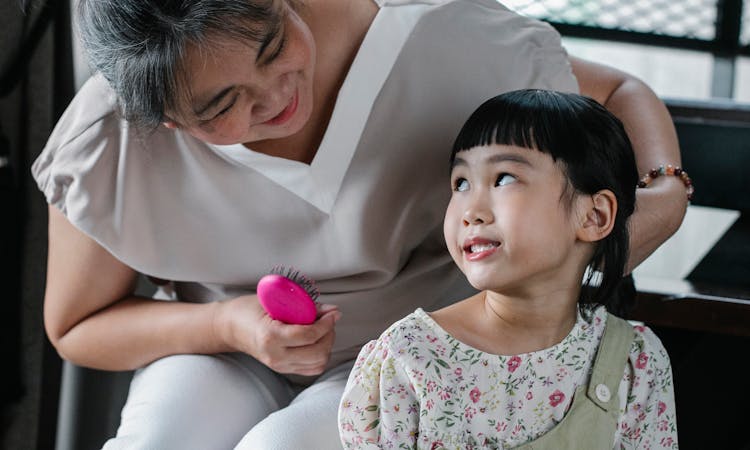 Loving Woman Brushing Hair Of Little Girl