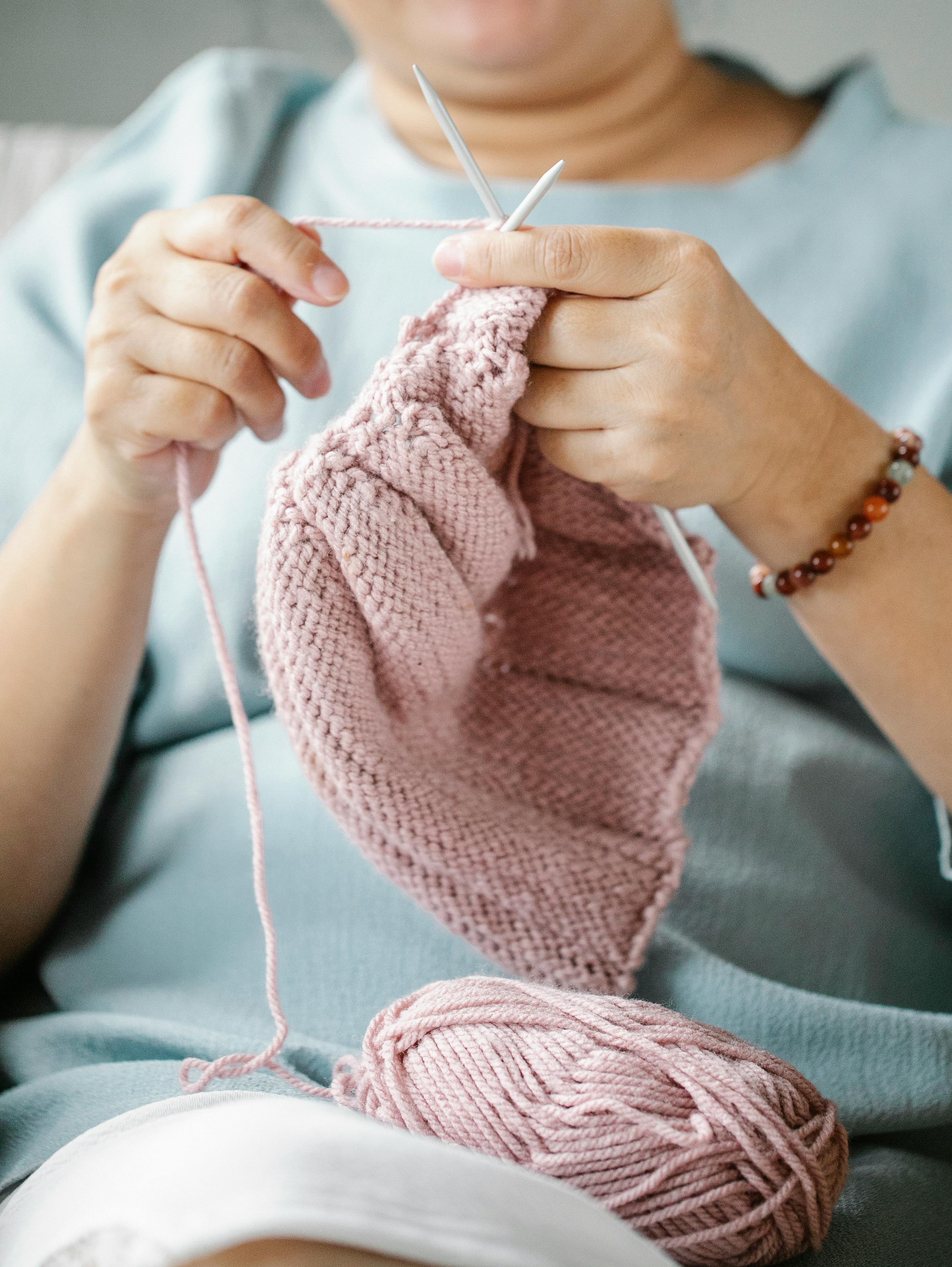 Faceless calm relaxed woman sitting with ball of pink yarn and knitting with needles